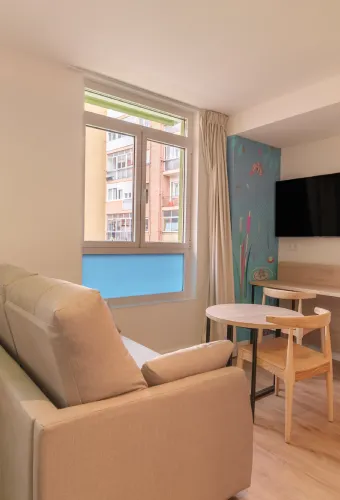 Sala moderna con sofá, mesa y sillas, ventana con vista, TV en la pared. Decoración minimalista.