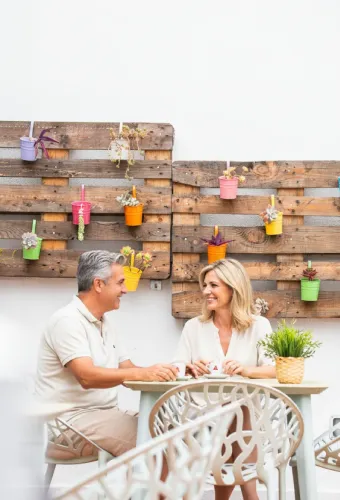 Pareja sentada en un café al aire libre con decoración de macetas coloridas en la pared.