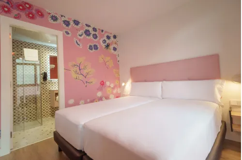 Habitación colorida con dos camas y mural floral en la pared, baño al fondo.