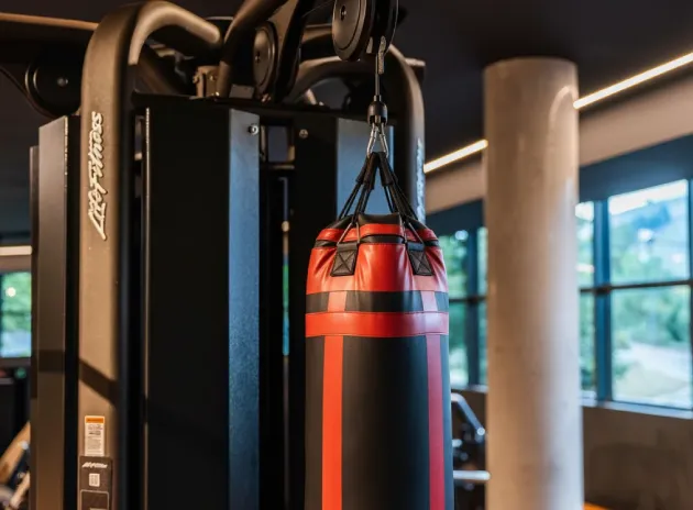Saco de boxeo colgado en un gimnasio, visto junto a una máquina de ejercicios.