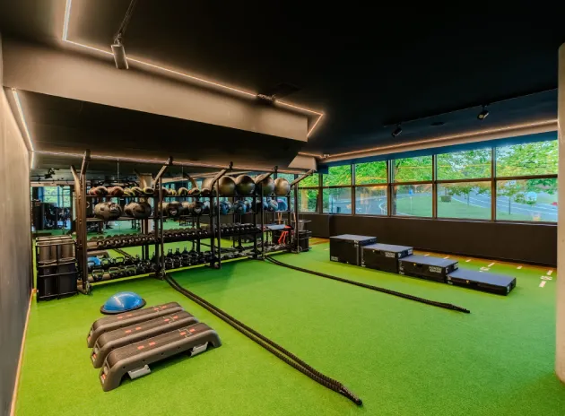Gimnasio moderno con equipo de entrenamiento funcional y césped artificial. Ventanas con vista exterior.