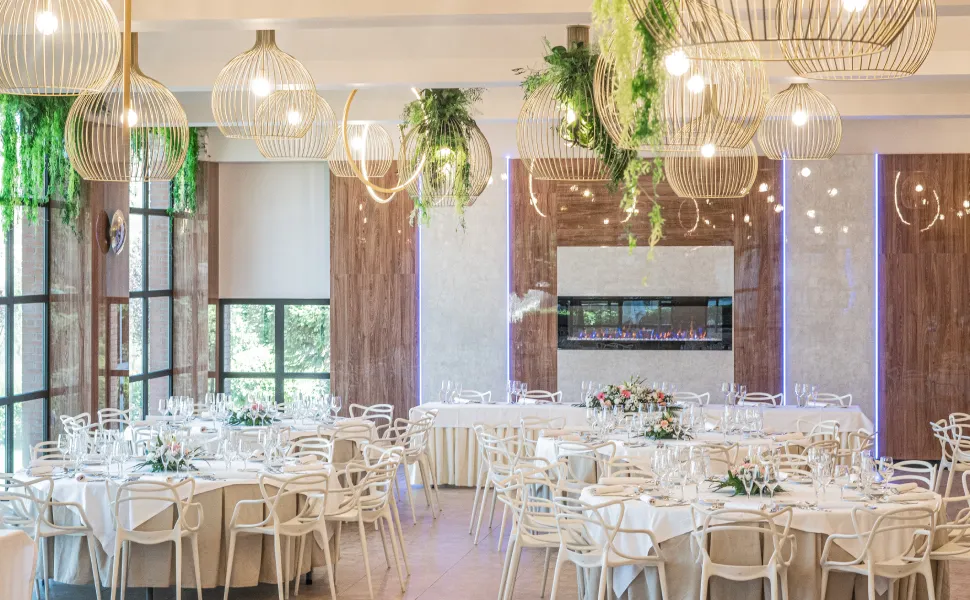 Salón de eventos elegante con mesas redondas decoradas y lámparas colgantes modernas.
