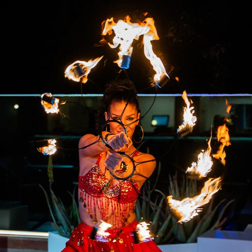 Una persona realiza un espectáculo de malabares con fuego, vestida con un traje rojo brillante.