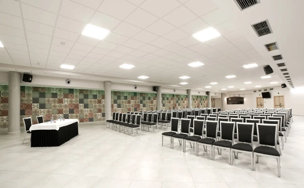 Sala de conferencias vacía con sillas negras y mesa al frente.