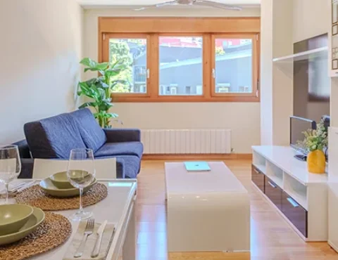 Sala moderna con sofá azul, mesa blanca, ventana grande y decoración sencilla.