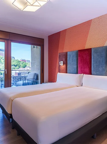 Habitación de hotel con dos camas individuales, balcón y vista a un parque.
