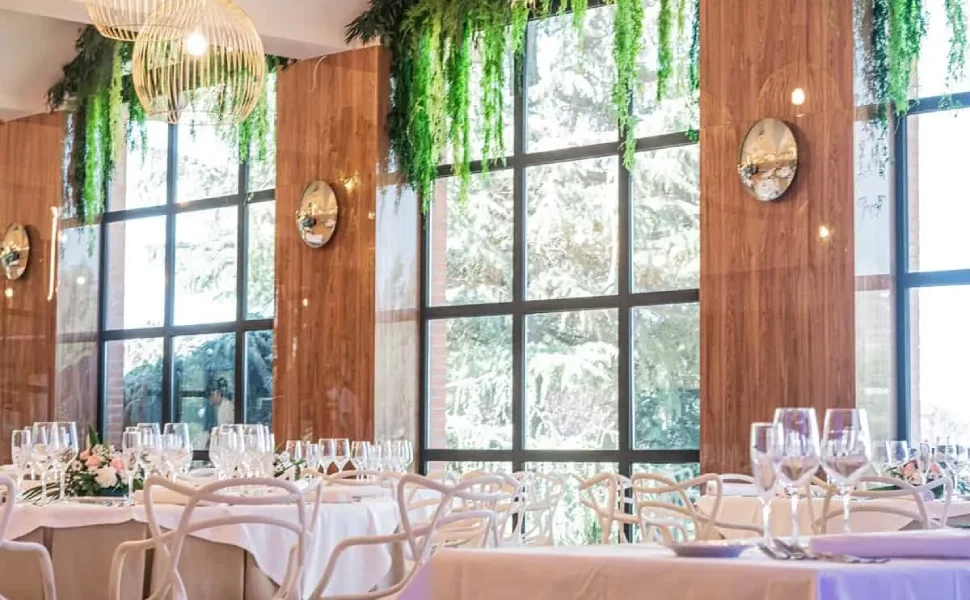 Sala elegante con mesas puestas y decoración verde colgante.
