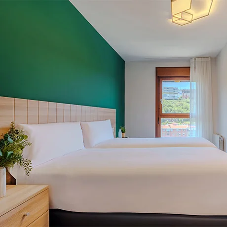 Habitación con dos camas, pared verde, ventana con cortina y decoración minimalista.