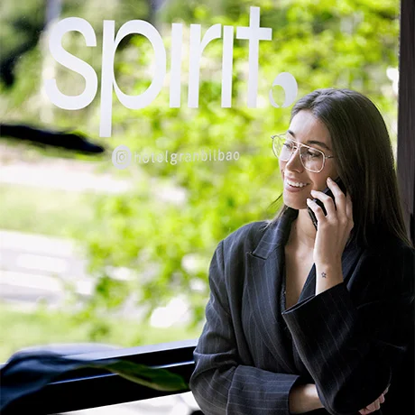 Mujer hablando por teléfono frente a una ventana con el texto "spirit" en un hotel.