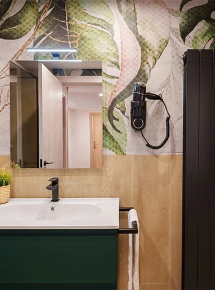 Baño moderno con papel tapiz floral, espejo, secador y lavabo con grifo negro.
