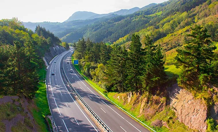 Carretera entre paisajes montañosos verdes con cielo despejado y algunos vehículos en circulación.