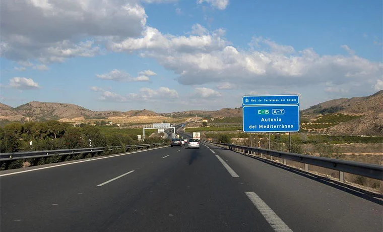 Carretera A-7 con cartel de "Autovía del Mediterráneo" y paisaje montañoso al fondo.