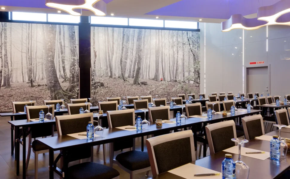 Sala de conferencias con mesas, sillas y decoración de bosque en la pared.