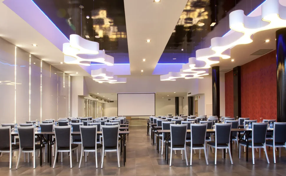 Sala de conferencias moderna con sillas, mesas y luces colgantes.