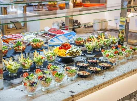 Buffet con variedad de ensaladas en recipientes de vidrio sobre una mesa.
