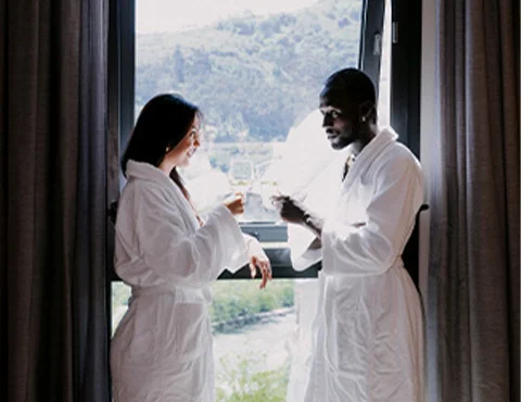 Personas en batas brindando frente a una ventana con vista a un paisaje verde.
