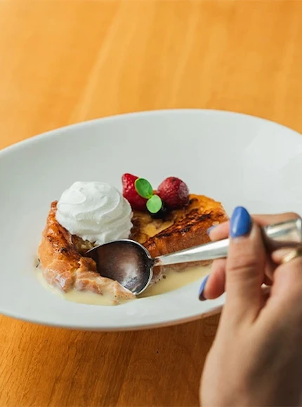 Postre con crema, fresas y cuchara en un plato blanco. Manos femeninas con uñas pintadas sostienen la cuchara.