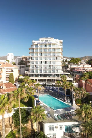Edificio de hotel moderno con piscina, rodeado de palmeras bajo un cielo despejado.