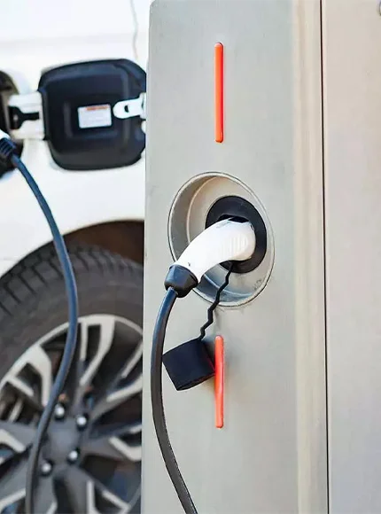 Cargador de vehículo eléctrico conectado a una estación de carga, con el coche al fondo.