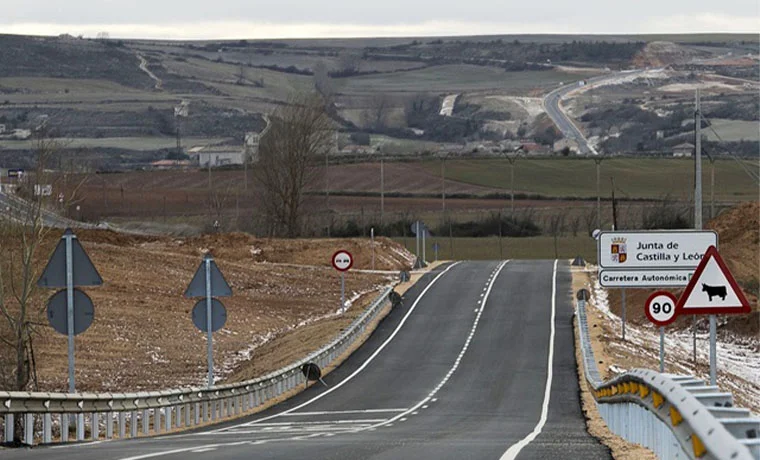Carretera desierta en Castilla y León, con señales y paisaje rural al fondo.