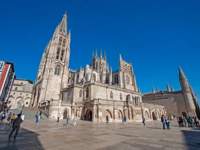 Catedral gótica con torres altas y múltiples pináculos, rodeada de personas bajo un cielo azul.