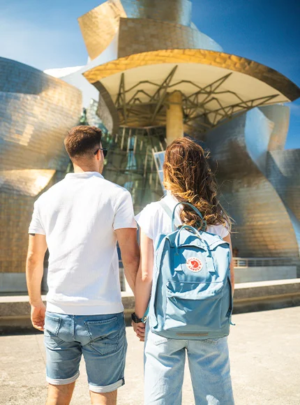 Pareja de espaldas frente al Museo Guggenheim Bilbao en un día soleado.