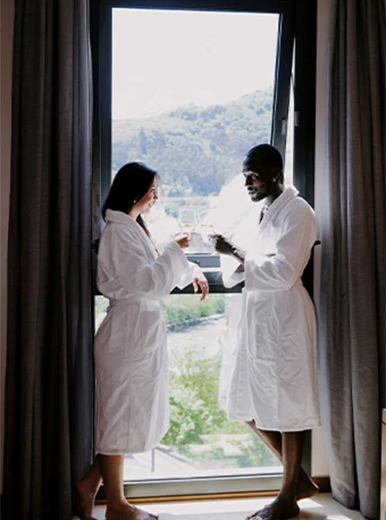 Dos personas en batas blancas brindan frente a una ventana con vista a un paisaje verde.