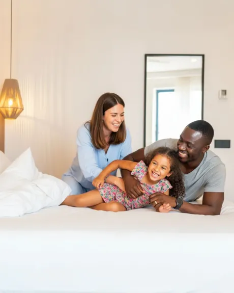 Una familia sonríe y juega sobre una cama en una habitación luminosa.