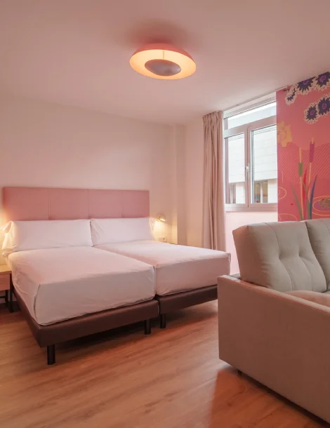 Habitación luminosa con dos camas, sofá, ventana y decoración floral.