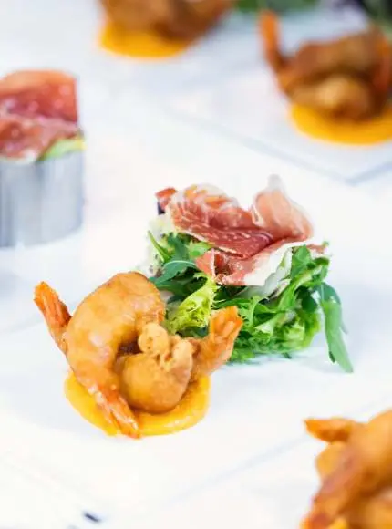 Camarones empanizados con puré, ensalada y jamón sobre un plato blanco.