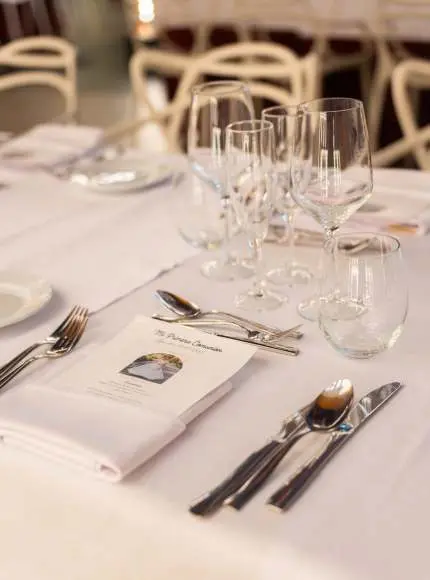 Mesa elegantemente puesta con copas, platos y cubiertos sobre un mantel blanco.