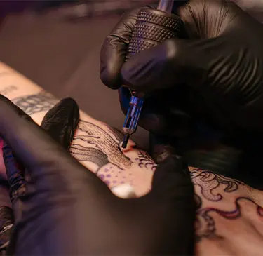 Primer plano de una mano tatuando un brazo con guantes negros.