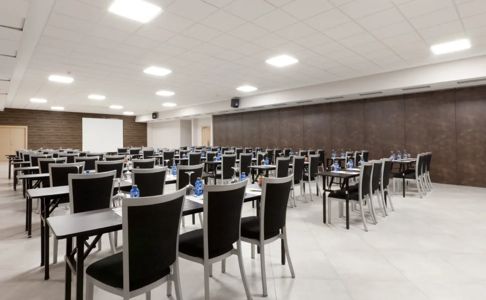 Sala de conferencias vacía con mesas y botellas de agua.