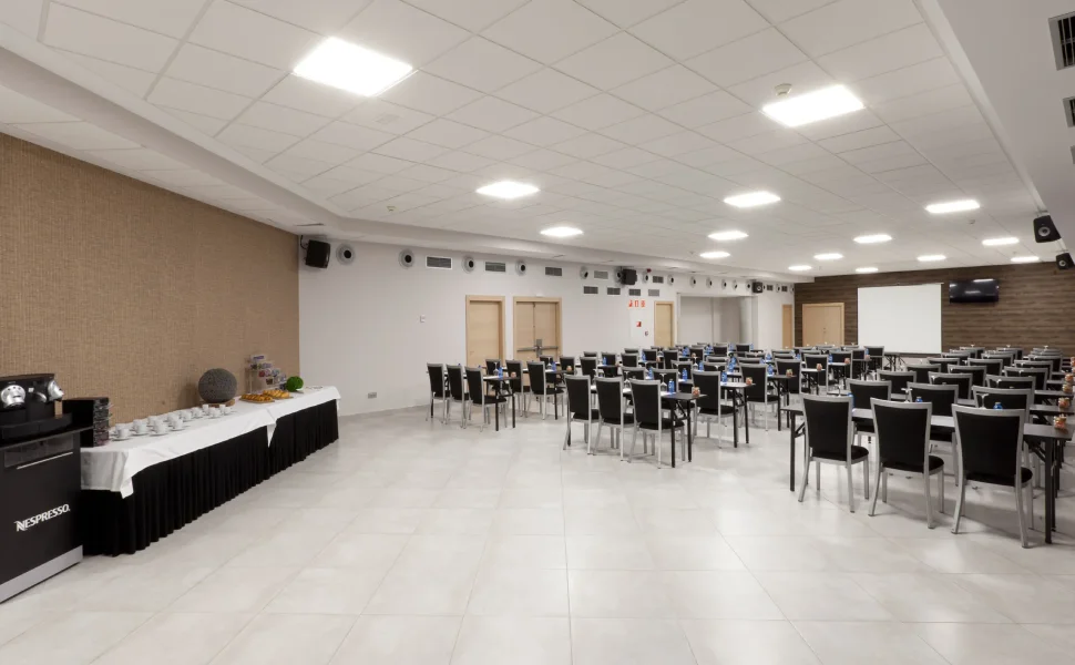Sala de conferencias con sillas y mesas, pantalla grande y mesa de café a un lado.