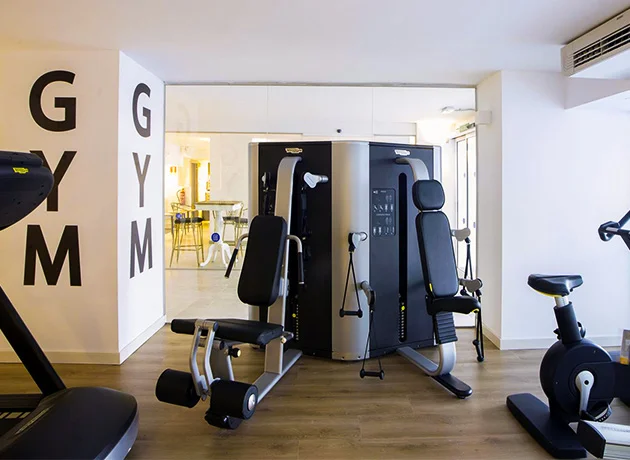 Gimnasio moderno con equipos de ejercicio como bicicleta y máquina de pesas en sala iluminada.