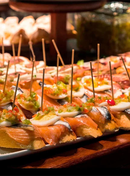 Pinchos variados con salmón y pimientos sobre pan, sostenidos con palillos.