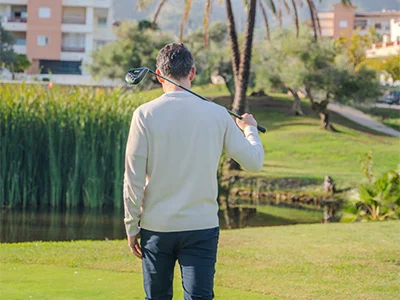 Hombre de espaldas en un campo de golf, sostiene un palo y mira hacia el paisaje.