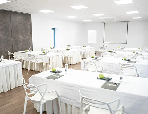 Sala de conferencias moderna con mesas blancas, sillas, pizarras y manzanas verdes.
