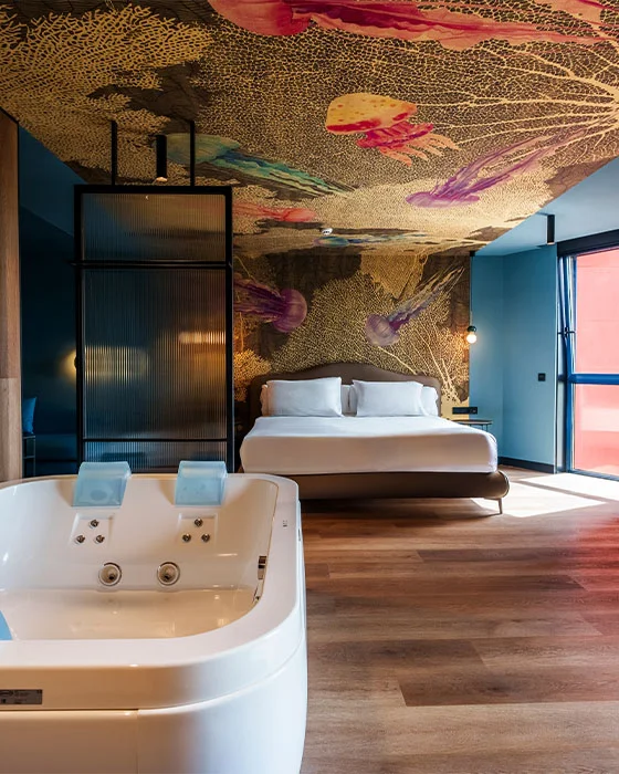 Habitación con jacuzzi, cama doble y techo decorado con medusas coloridas.