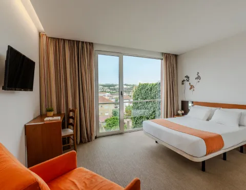 Habitación de hotel moderna con cama doble, ventana grande, TV y decoración minimalista.