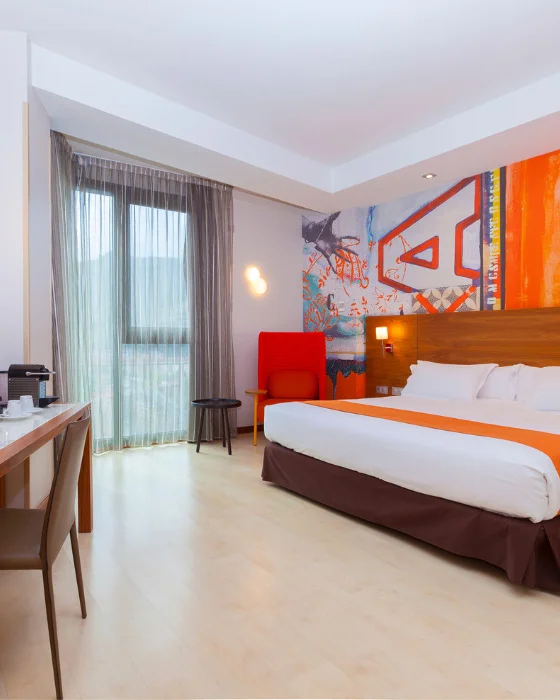 Habitación de hotel moderna con cama grande, obra de arte en la pared y ventana con cortinas.