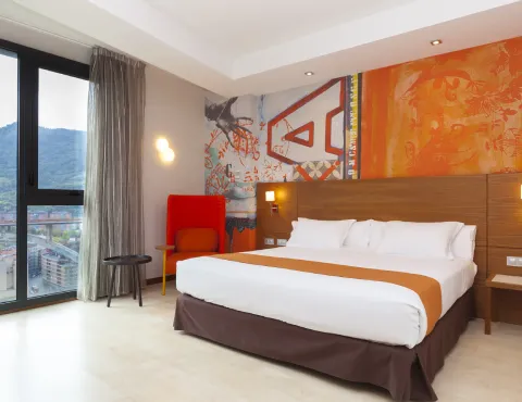 Habitación moderna con cama doble, decoración colorida y vista a la montaña por la ventana.