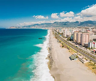 Playa y ciudad costera con montañas al fondo y cielo despejado.