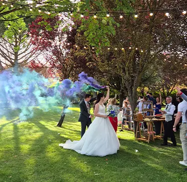 Novios celebran al aire libre con humo de colores y luces colgantes.