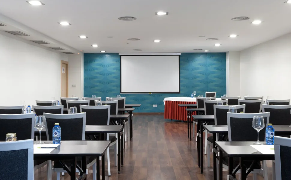 Sala de conferencias con sillas, mesas y pantalla de proyección.