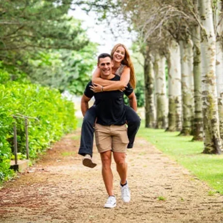 Pareja sonriendo, él lleva a ella en la espalda por un camino arbolado.