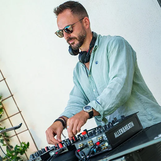 Hombre con gafas y audífonos tocando en una consola Allen & Heath.