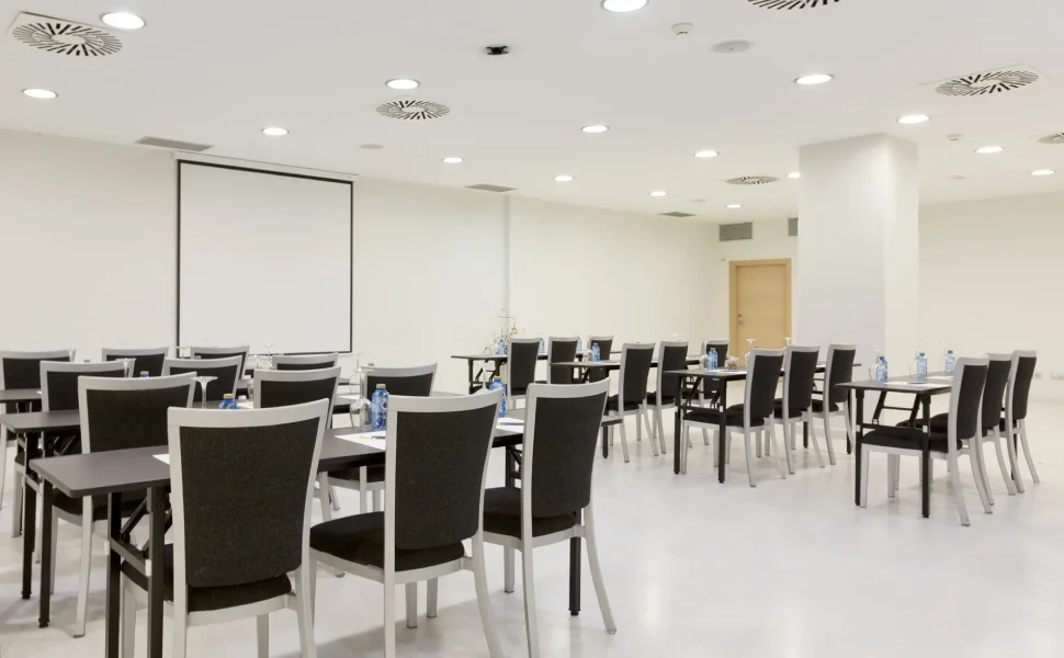 Sala de conferencias con sillas, mesas y una pantalla al frente.
