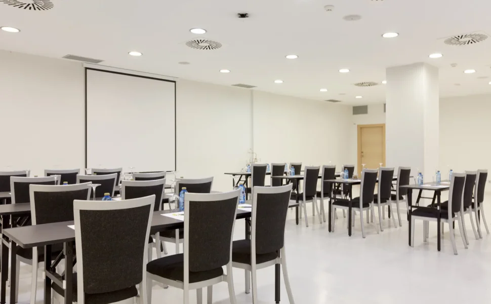 Sala de conferencias vacía con sillas negras y proyector.