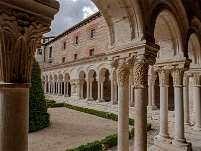 Claustro antiguo con arcos y columnas en un edificio de piedra, cielo nublado.